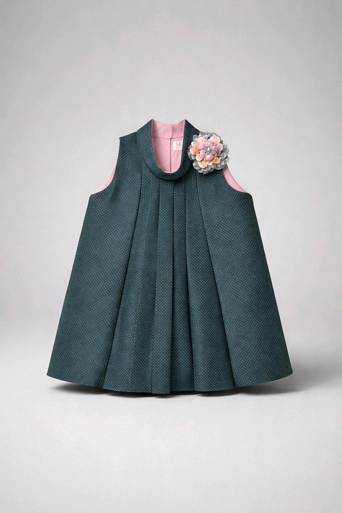 A sleeveless dark teal pleated dress with a pink inner lining and a decorative multicolor floral embellishment on the left shoulder.