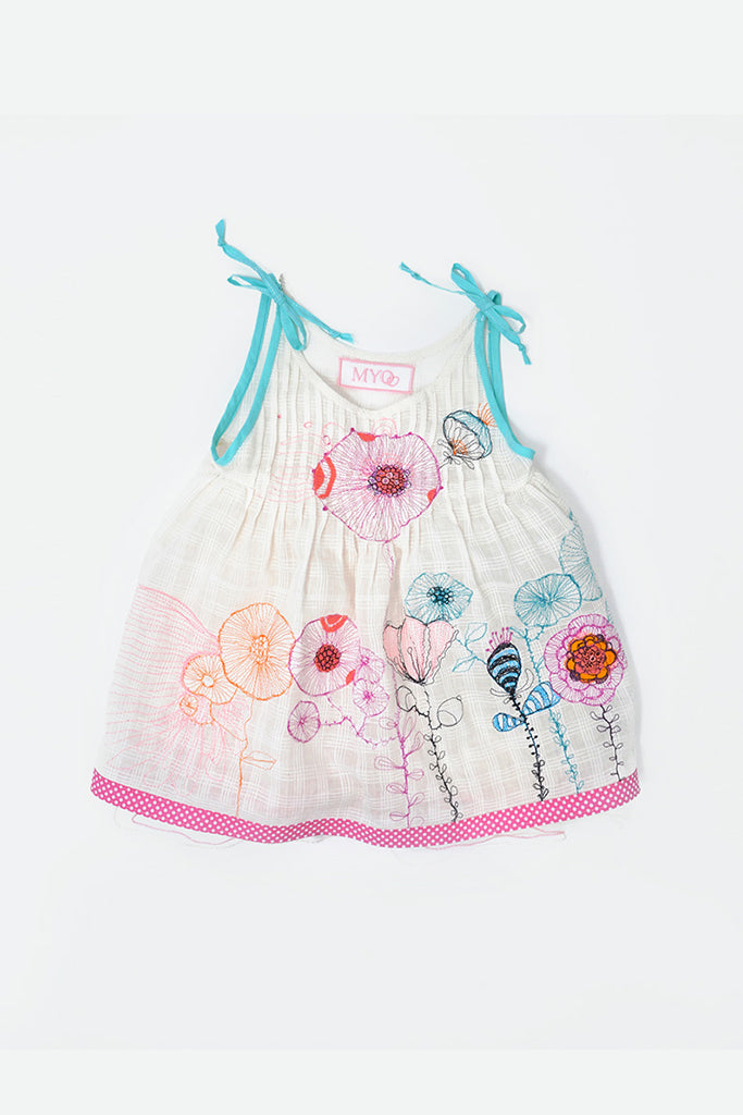 A white sleeveless baby dress with colorful floral embroidery, turquoise tie straps, and a pink polka dot hem.