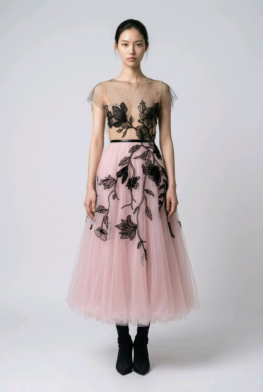 Model wearing a pink dress with black floral embroidery.
