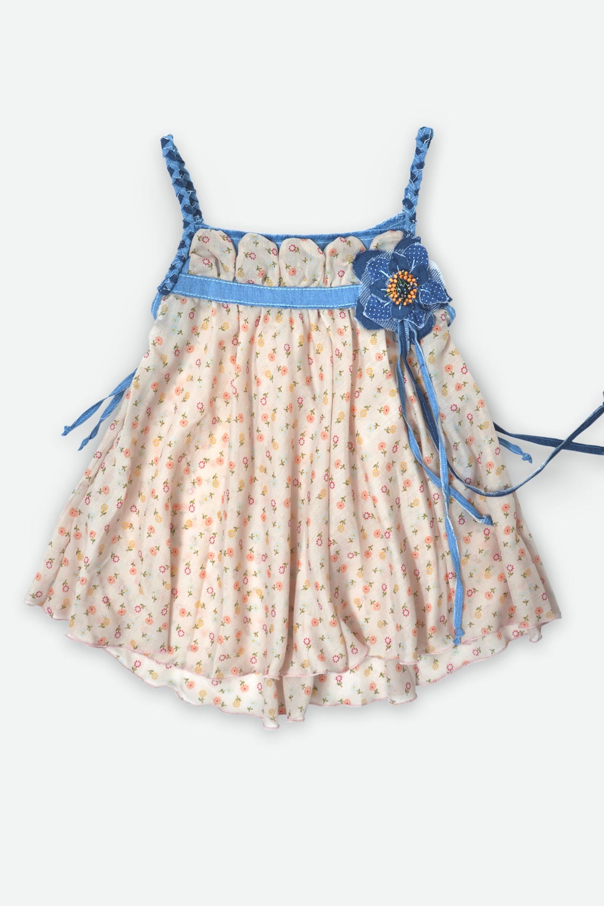 A toddler girl's sleeveless romper dress featuring a cream-colored body with a small orange and blue floral pattern, a blue waistband, braided blue shoulder straps, and a blue fabric flower applique with a gold center on the left side.