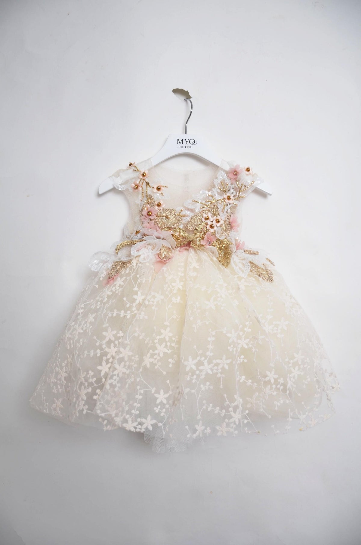 A toddler girl's formal party dress in cream tulle with white floral embroidery, pink floral accents, and gold glitter details.