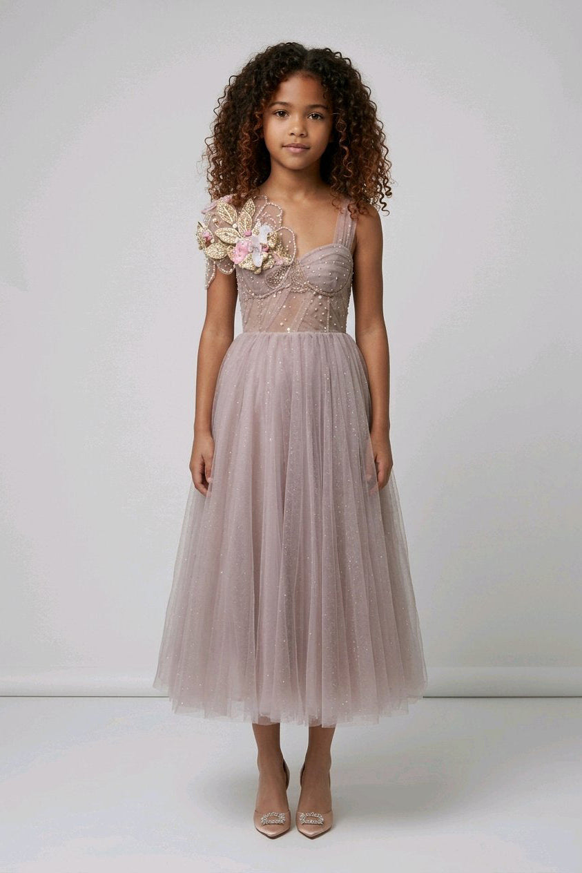 A young girl wearing a sleeveless dusty pink tulle dress with floral applique on the bodice.