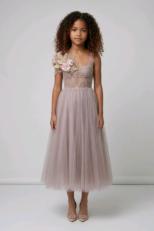 A young girl wearing a sleeveless dusty pink tulle dress with floral applique on the bodice.