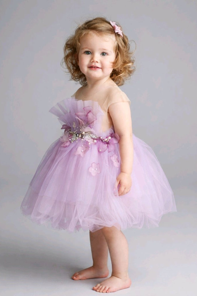 A toddler girl wearing a light purple tulle dress with a floral waistband.