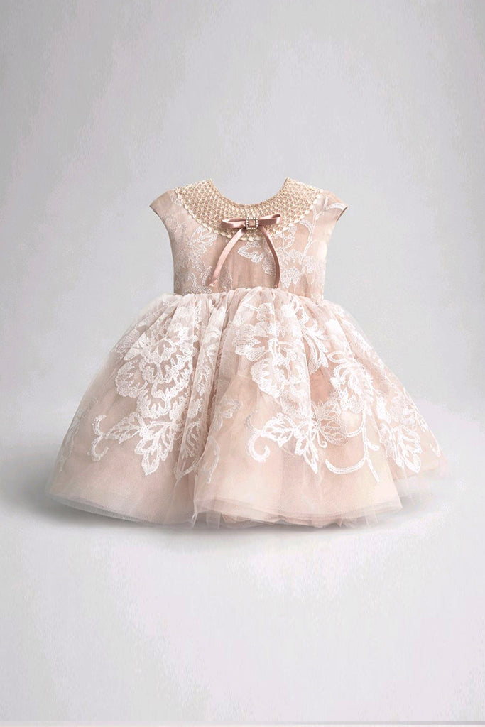 A toddler girl's formal party dress in a soft blush nude tulle with white floral lace overlays, featuring a crew neck with pearl-like embroidery, a brown satin bow, and cap sleeves.