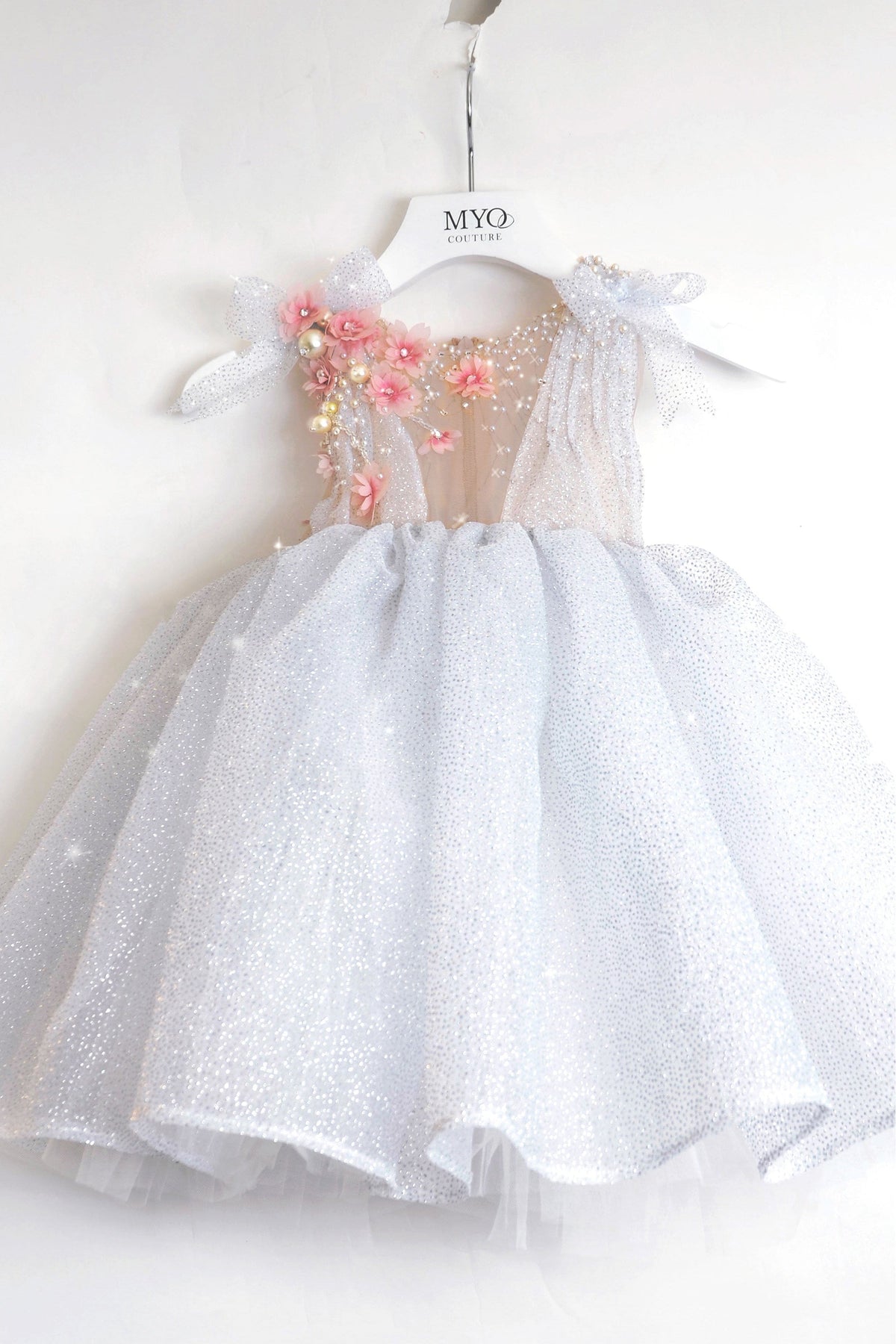 The dress features a sparkly silver tulle skirt, a sheer mesh bodice, and pink floral embellishments with gold beads on the left side.