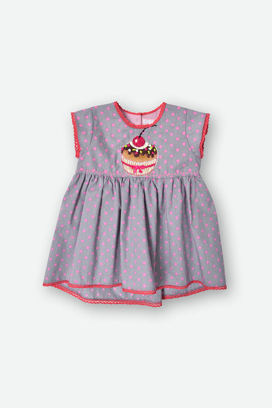 A baby girl's sleeveless dress in a dusty lavender-gray fabric with pink polka dots, featuring a cupcake graphic on the chest and coral trim.