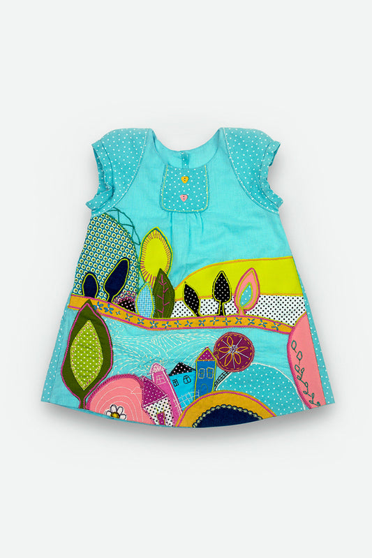 A sleeveless dress in light blue with a colorful patchwork-style landscape embroyderi featuring trees, hills, and houses in pink, yellow, green, and blue.